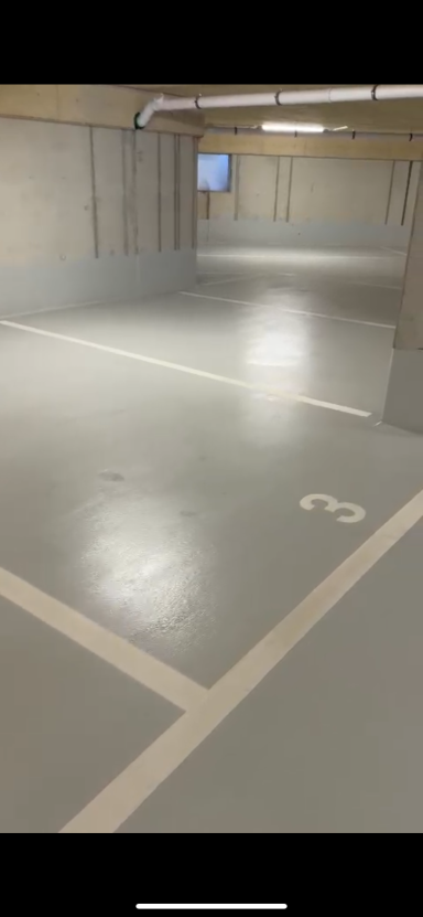 Leerer Parkhausbereich mit grauem Boden und markierten Parkplätzen.